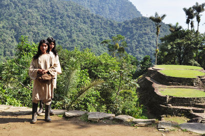 Young woman standing by tree against mountain