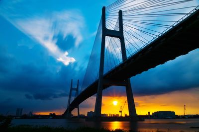 Low angle view of suspension bridge over river during sunset