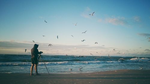 Man photographing against birds flying at beach