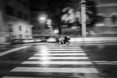 Blurred motion of people riding motorcycle on illuminated street in city at night