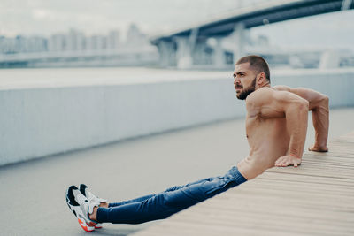 Side view of shirtless young man exercising on bridge