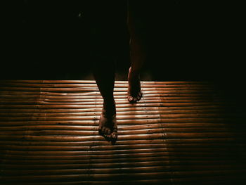 Low section of woman standing on bamboo mat in dark