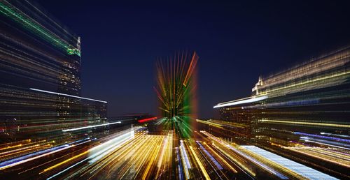 Light trails on illuminated city buildings against clear sky at night