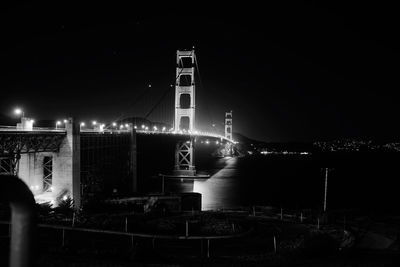 Illuminated bridge and buildings against sky at night