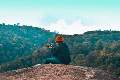 Man sitting on rock looking at mountains against sky