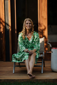 Portrait of a smiling young woman sitting on chair waiting to get her wedding dress on