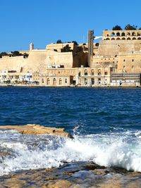 Buildings by sea against clear blue sky