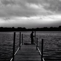 Silhouette man standing on pier over lake against sky