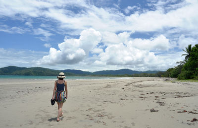 Rear view of woman walking on shore at beach against sky