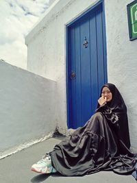 Portrait of young woman sitting against blue wall