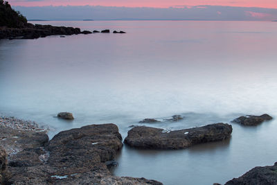 Rocks by sea against sky during sunset