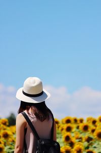 Rear view of woman standing by sunflower field against sky