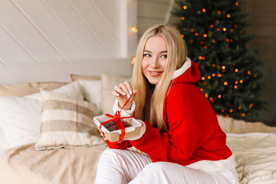 Smiling woman holding gift box while sitting on bed
