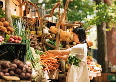 Rear view of woman picking vegetables for sale at market