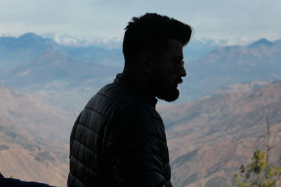 Young man wearing sunglasses against mountain ranges and sky