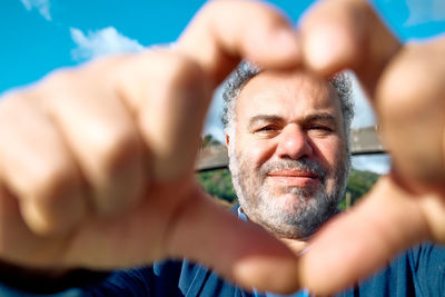 Happy sincere middle aged bearded man making heart gesture with fingers, showing love. 