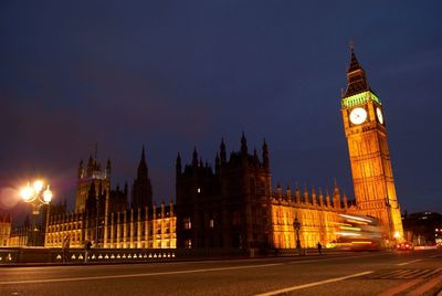 City street by illuminated big ben and houses of parliament against sky at night