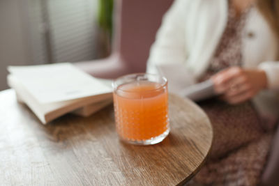 Lifestyle photo of drink and book on the wooden table of cafe. unrecognizable woman reading a book