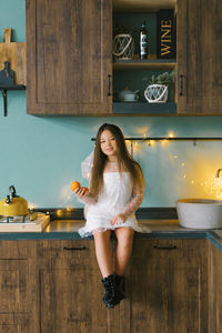 Portrait of a cheerful little girl with tangerines in her hands in the christmas kitchen, cozy home