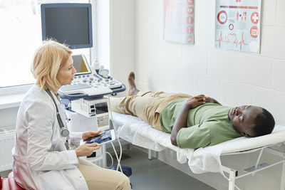 Doctor talking with patient lying on bed doing ultrasound in clinic