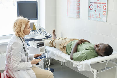 Doctor talking with patient lying on bed doing ultrasound in clinic