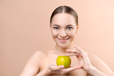 Portrait of young woman holding apple against pink background