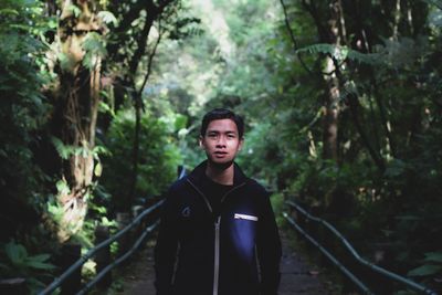 Portrait of young man standing amidst plants in forest