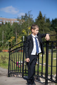 Young man standing by railing against trees