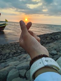 Midsection of person holding sea against sky during sunset