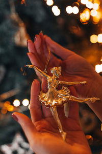 Female hands holding a golden tiny figurine christmas toy of a ballerina. magic winter details
