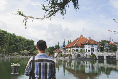 Rear view of man by lake against building