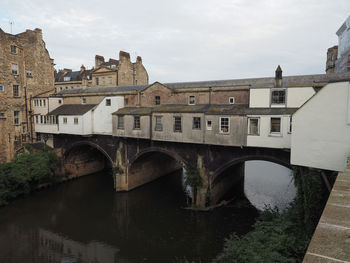 Arch bridge over river by buildings against sky