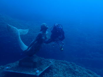 Man scuba diving by sculpture in sea