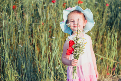 Full length of cute girl holding flower while standing on grass