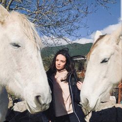 Portrait of young woman standing by horse against sky