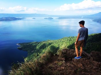 Rear view of young man standing on mountain by sea