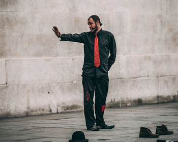 Full length of young man looking at camera while standing against wall