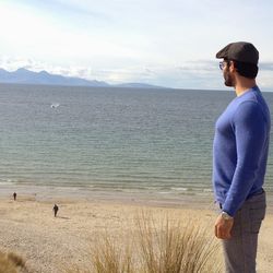 Side view of man standing at beach looking at sea against sky