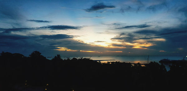 Silhouette trees by sea against sky during sunset