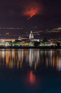 Illuminated buildings by river against sky at night