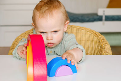 Littleboy plays with rainbow colored wooden toys at white table. cozy room background. eco lifestyle