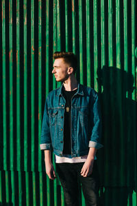 Young man looking away while standing against wall