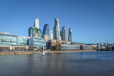 Buildings by sea against clear blue sky