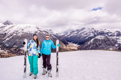 Portrait of smiling friends with snowboards standing on snowcapped mountain against sky