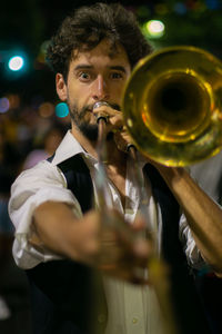 Portrait of young man holding camera while standing at night