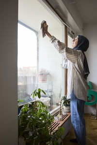 Woman in headscarf cleaning windows at home