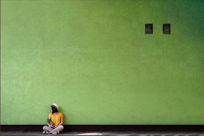 Side view of woman with pineapple sitting against green wall