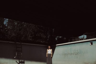 Woman standing by swimming pool at night