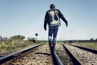 Man walking on railroad track against clear blue sky