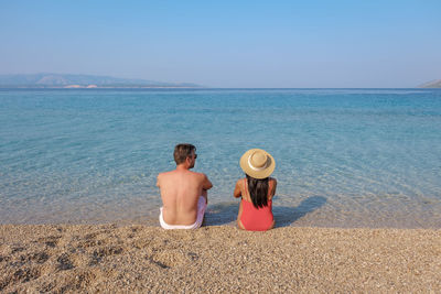 Rear view of woman sitting at beach against clear sky